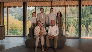 Gastgeberfamilie des Familienhotels Engel Gourmet und Spa vor Panoramafenstern mit Blick auf die Berge.