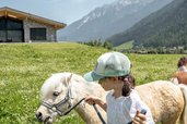 Mädchen führt ein weißes Pony an der Leine über eine Wiese beim Familienhotel Kindl.