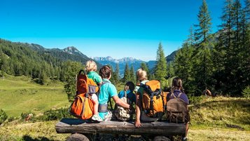 Eine fünf-köpfige Familie sitz auf einer Bank und schaut in die Berge im Salzburger Land.