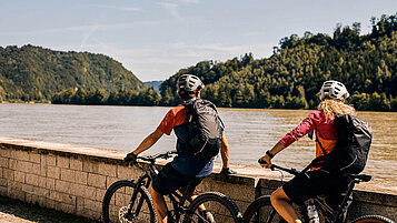 Zwei Fahrradfahrer fahren auf einem Weg an einem See in Obernzell im Bayerischer Wald.