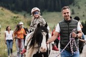 Ein Kind mit bemaltem Gesicht reitet im Familienhotel Tirolerhof auf einem Pony durch die Natur, begleitet von einem Erwachsenen