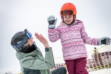 Im Familienhotel Elldus im Erzgebirge freut sich ein Kind beim Skifahren über ein High-Five mit der Skilehrerin.