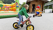 Junge fährt draußen auf dem Dreirad im Rahmen der Kinderbetreuung des Familienhotels Egger.
