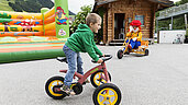 Junge fährt draußen auf dem Dreirad im Rahmen der Kinderbetreuung des Familienhotels Egger.