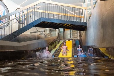 Drei Kinder rutschen fröhlich die bunte Trio Slide Rutsche im Alpenhotel Kindl im Sutbaital hinunter