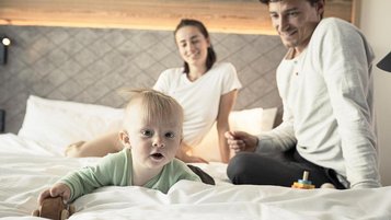 Vater und Mutter sitzen gemeinsam mit ihrem Baby auf den Bett und genießen ihren Familienurlaub