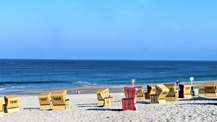 Gelbe und rote Strandkörbe an einem Nordseestrand in Deutschland.