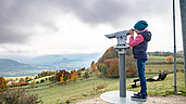 Wandern in der Rhön auf dem "Schöpfungsweg: Kind sieht durch ein Fernrohr ins Tal