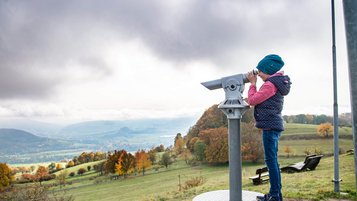 Wandern in der Rhön auf dem "Schöpfungsweg: Kind sieht durch ein Fernrohr ins Tal