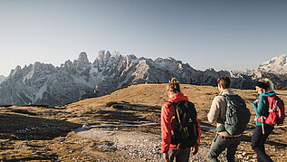 Eine Bergkette ziert den Hintergrund. Freunde beim Wandern in Südtirol im Sommer blicken auf das Naturspektakel.