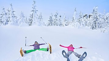 Zwei Frauen liegen im Tiefschnee mit Scheeschuhen an den Füßen.