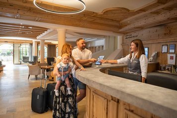 Familie mit Kleinkind beim Check-in an der Rezeption des Familienhotels Alpenhotel Kindl mit freundlicher Mitarbeiterin.