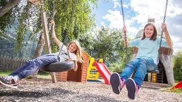 Kinder schaukeln auf dem Spielplatz im Familienhotel Kinderhotel Sailer in Pitztal.