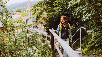 Salzburger Land Ausflugstipps: Eine Frau wandert auf dem Gasteiner Wasserfall. Im Hintergrund ist ein Kirchturm zu sehen.