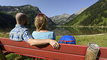 Gemütlich die Natur bestaunen: ein Paar auf einer Bank genießt den Blick auf den See in Tirol.