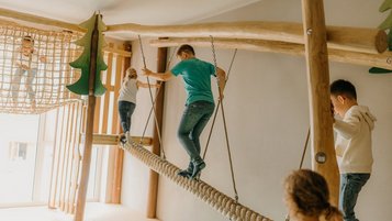 Im Spielbereich des Familienhotel Friedrichshof balancieren Kinder auf einer Hängebrücke aus Seilen.