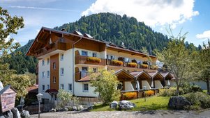 Hauptgebäude des Familienhotels Krone im Allgäu mit blumengeschmückten Balkonen und Blick auf die Allgäuer Berge.