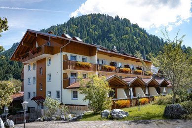 Hauptgebäude des Familienhotels Krone im Allgäu mit blumengeschmückten Balkonen und Blick auf die Allgäuer Berge.