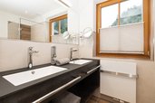 Modernes Badezimmer im Familienhotel Oberkarteis mit Doppelwaschbecken, großer Dusche und Blick auf die Berglandschaft.