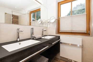 Modernes Badezimmer im Familienhotel Oberkarteis mit Doppelwaschbecken, großer Dusche und Blick auf die Berglandschaft.