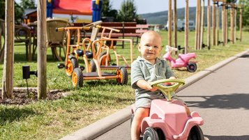 Ein kleiner Junge fährt draußen mit dem Bobbycar auf der Fahrzeugrennstrecke des Familienhotels Rhön Feeling. Spiel und Spaß sind in eurem Familienurlaub in der Rhön garantiert.