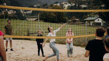 Eine Familie spielt auf einem Sandplatz vor bergiger Kulisse Beachvolleyball im Außenbereich des Hotel Sonngastein im Salzburger Land.