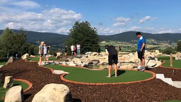 Minigolfanlage im Böhmerwaldpark mit spielenden Gästen, Felsenhindernissen und Blick auf die Hügellandschaft.