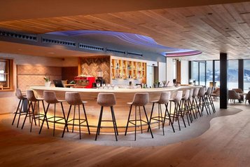 Große Bar mit Barhockern, schöner Beleuchtung und Panoramafenstern im Familienhotel Allgäuer Berghof.