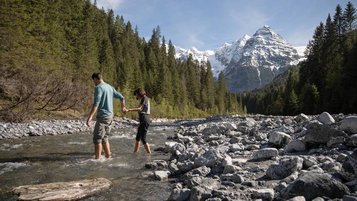 Familie wandert nahe dem Familienhotel Bella Vista in Südtirol an einem Bachbett mit Bergpanorama.