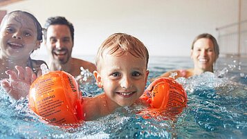 Eine junge Familie hat viel freude beim Schwimmen im Indoorpool des Familienhotels Das Hopfgarten in Tirol.