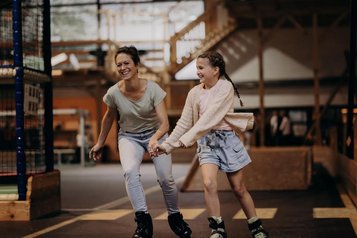 Eine Mutter fährt mit ihrer Tochter in der Erlebnishalle des Hotel Sonngastein im Salzburger Land Inlineskates.