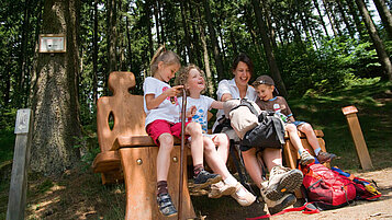 Familie beim Wandern auf dem Liebesbankenweg im Harz. Die Familie pausiert auf einer Bank.