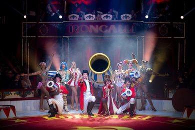 Zirkusensemble feiert in der Manege unter buntem Konfettiregen vor applaudierendem Publikum.