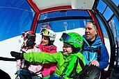 Familie mit zwei Kindern sitzt mit Skibekleidung ausgerüstet in einer Gondel im Familienurlaub in Tirol.