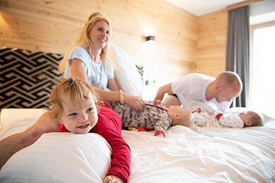 Familie mit drei Kindern tobt auf dem Bett im Familienzimmer des Familienhotels Landgut Furtherwirt in Tirol.
