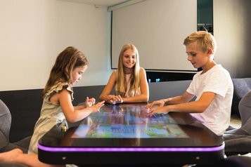 Drei Kinder spielen gemeinsam ein interaktives Tischspiel im Almfamilyhotel Scherer in Tirol