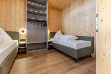 Heller Kinderschlafbereich im Familienhotel Almfamilyhotel Scherer mit zwei Einzelbetten, Holzverkleidung und modernen Lichtelementen.