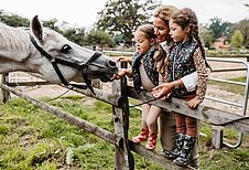Mutter streichelt mit ihren beiden Töchtern ein Pferd auf dem Reitergelände des Familienhotels Landhaus Averbeck in der Lüneburger Heide.