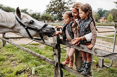 Mutter streichelt mit ihren beiden Töchtern ein Pferd auf dem Reitergelände des Familienhotels Landhaus Averbeck in der Lüneburger Heide.