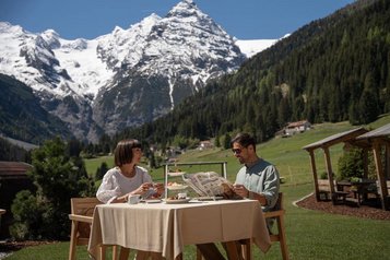 Eltern sitzen bei einer Mahlzeit im Außenbereich des Restaurants und genießen den Blick auf die Berge im Hotel Bella Vista in Südtirol.