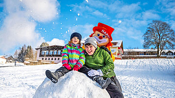 Kinder spielen im Schnee auf dem Hotelgelände mit Clown Happy im Familienhotel Mein Krug.