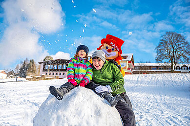 Kinder spielen im Schnee auf dem Hotelgelände mit Clown Happy im Familienhotel Mein Krug.