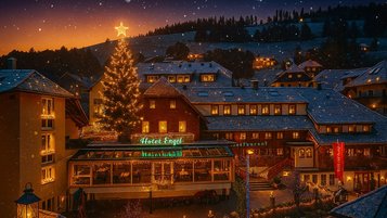 Das festlich beleuchtete Familienhotel Engel im Schwarzwald mit großem Weihnachtsbaum und verschneiter Winterlandschaft bei Sonnenuntergang.