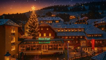 Das festlich beleuchtete Familienhotel Engel im Schwarzwald mit großem Weihnachtsbaum und verschneiter Winterlandschaft bei Sonnenuntergang.