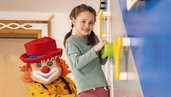 Kinder klettern an der Kletterwand im Happy-Club des Familienhotels Alpenhotel Kindl in Tirol. Auch Clown Happy, das Maskottchen des Familienhotels, klettert mit und bringt die Kinder zum Lachen.