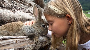 Mädchen kuschelt mit einem Hasen auf dem Hotelgelände des Familienhotels Kindl in Tirol