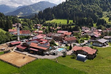 Luftaufnahme des Familienhotels Krone im Allgäu mit Blick auf Reitplatz, Pool und umliegende Natur.
