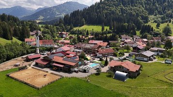 Luftaufnahme des Familienhotels Krone im Allgäu mit Blick auf Reitplatz, Pool und umliegende Natur.