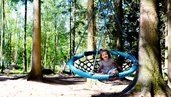 Ein Kind lacht uns sitzt in einer Nestschaukel im Waldspielplatz im Familienhotel Ulrichshof im Bayerischen Wald