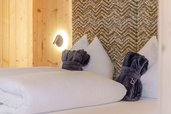 Gemütliches Doppelbett mit weißen Kissen und gefalteten Bademänteln im Familienhotel Almfamilyhotel Scherer in Osttirol.